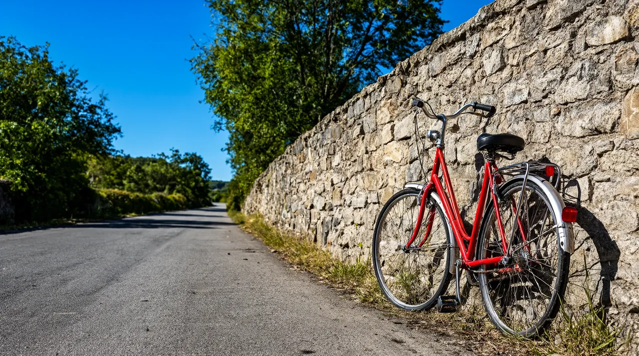 Una bicicleta roja antigua apoyada en un muro de piedra al inicio de un camino rural.
