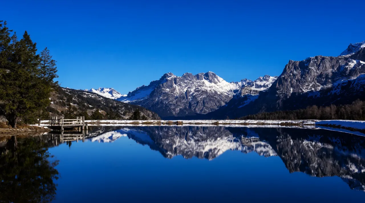 Un lago de montaña en calma que refleja las cumbres nevadas bajo el cielo azul