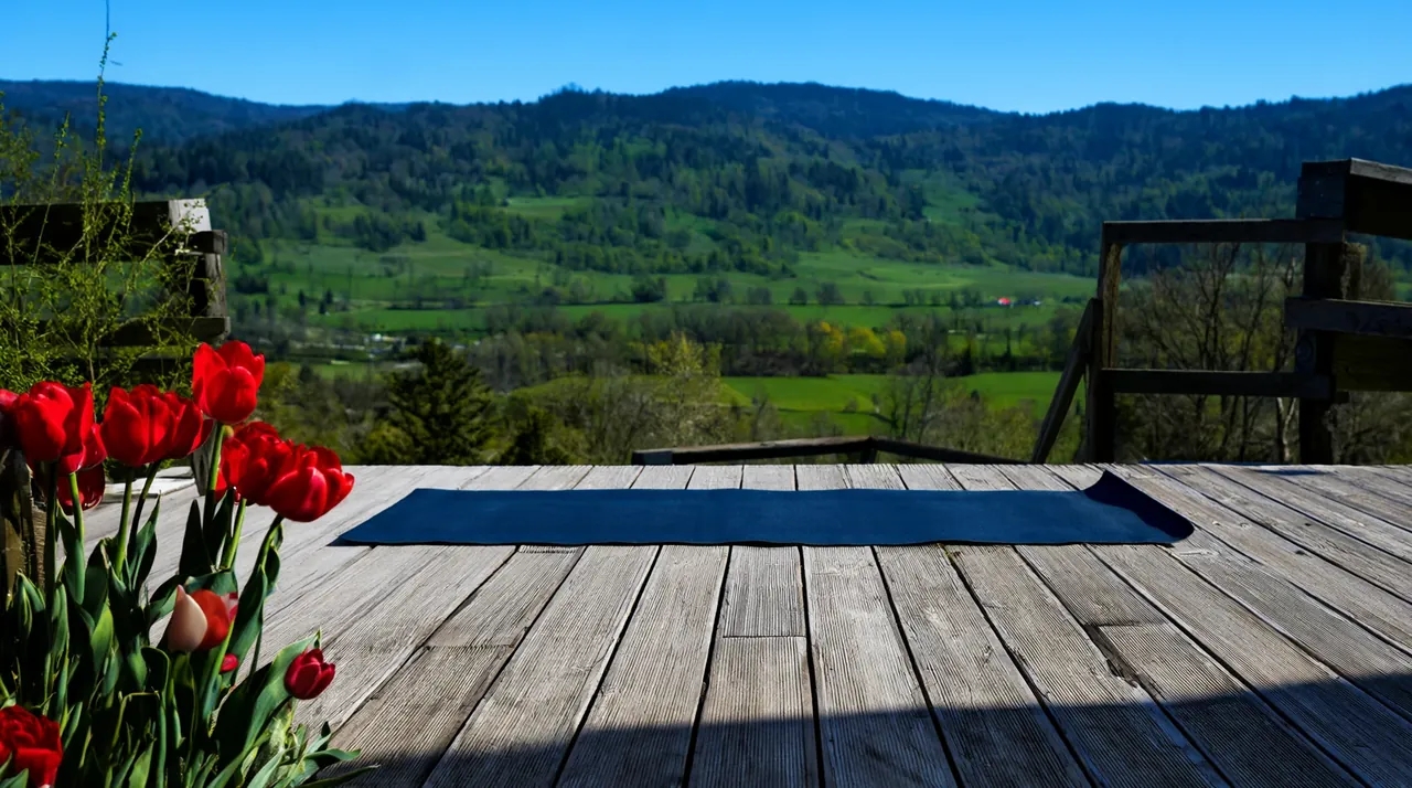 Una esterilla sobre una tarima de madera frente a un valle verde, con tulipanes rojos