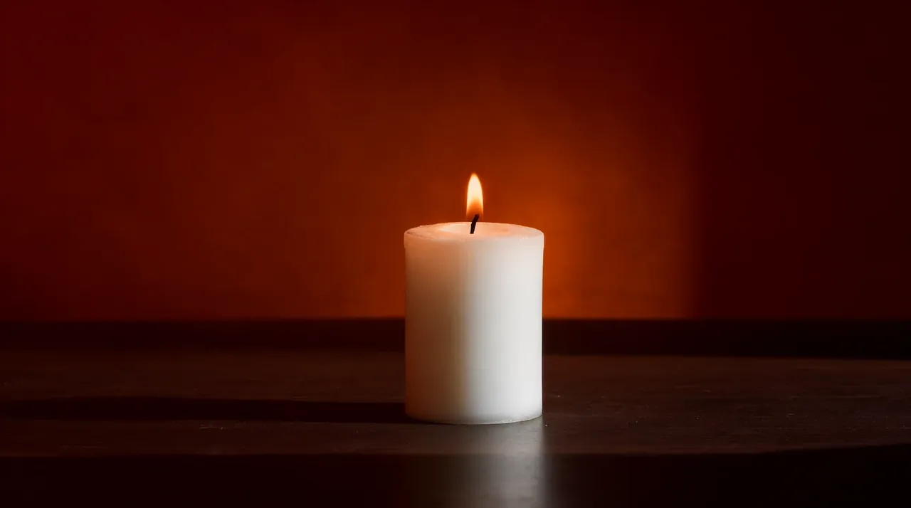 Una vela blanca encendida con una llama quieta sobre una mesa de madera.