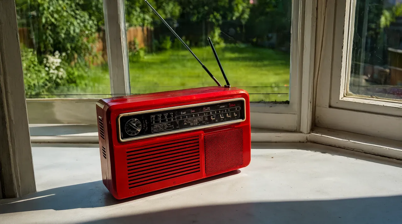 Una radio antigua roja con la antena extendida en el alféizar de una ventana soleada.